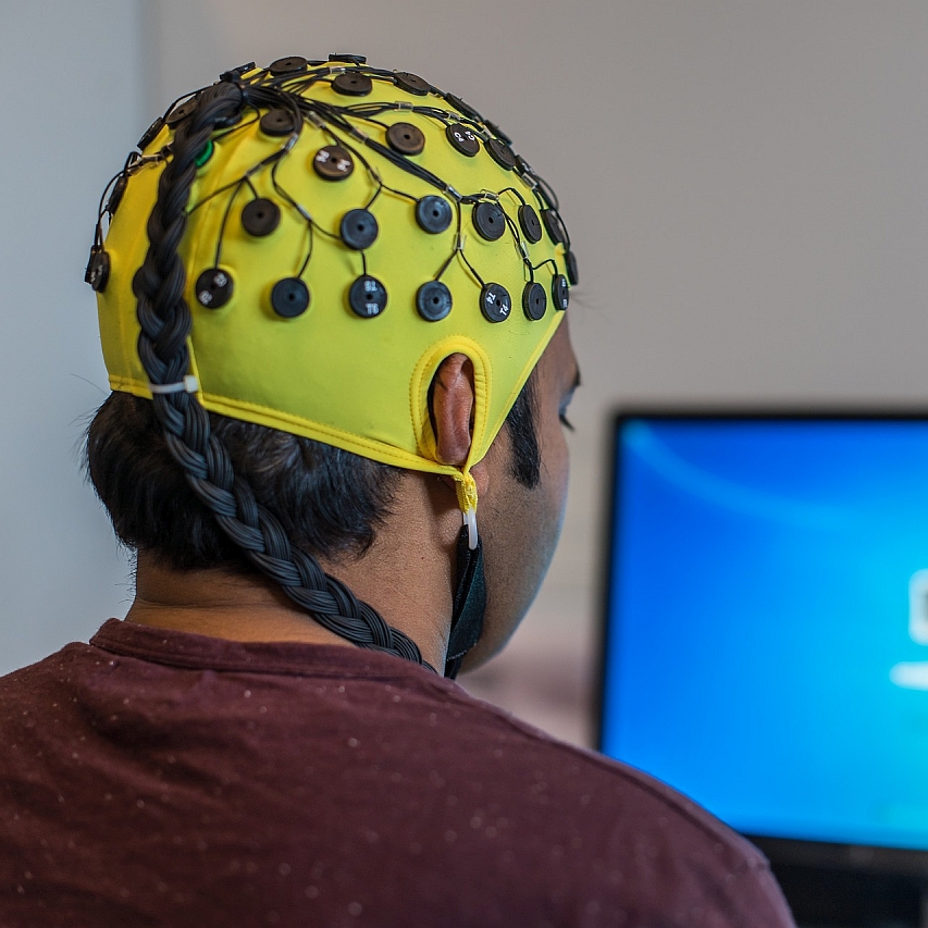 Man facing a computer with yellow EEG skullcap on